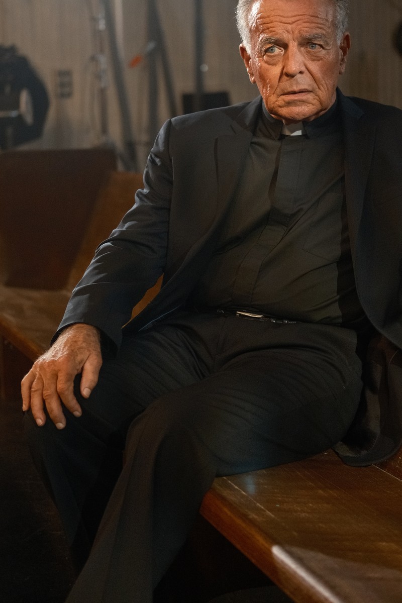 Ray Wise as the Pastor, grey-haired in his clerical collar in the dim of the church