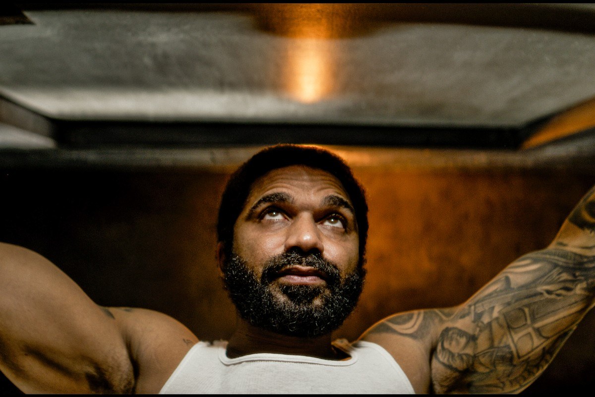 Dom lies in his bunk in the cell, lit by a narrow shaft of institutional light